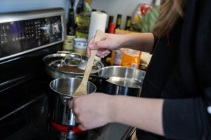Katelyn Moir stirs sauces on a stovetop, a close-up of her hands.