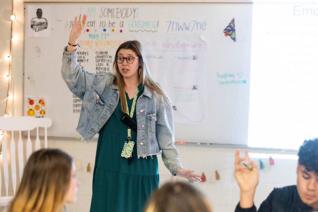 Madi Tyree holds her hand up in the air at the front of her classroom, as she teaches in her family and consumer sciences class 