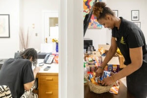 Cameron Goulde organizes something in the office, while Nafi Thiam puts out treats for an event on either side of a doorway