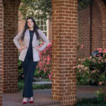 Lexie Lama poses outside on the sidewalk by the library, standing next to one of the brick pillars Lexie Lama poses outside on the sidewalk by the library, standing next to one of the brick pillars
