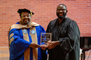 Charles E. Gibson III presents an awarda to Scott Cooper. They're posing together, holding Scott's plaque 