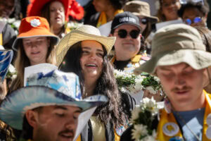 A group of students, several in their robes and button-covered stoles, sing during Daisy Chain
