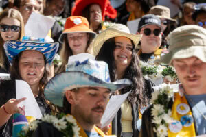 A group of students, several in their robes and button-covered stoles, sing during Daisy Chain