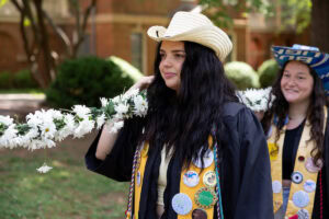 A group of seniors from the Class of 2025 walk and sing while holding the Daisy Chain