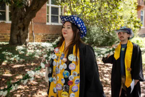 A group of seniors from the Class of 2025 walk and sing while holding the Daisy Chain