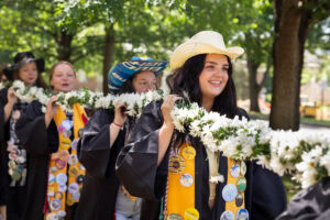 A group of seniors from the Class of 2025 walk and sing while holding the Daisy Chain
