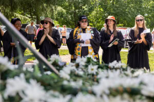 A group of students, several in their robes and button-covered stoles, sing during Daisy Chain