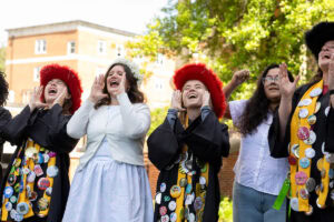 A group of students, several in their robes and button-covered stoles, sing during Daisy Chain