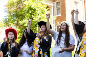 A group of students sing with their hands in the air during Daisy Chain