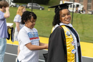 Sonia Langhorne '25 smiles as her son, acting as her squire, helps her with her hood during Commencement