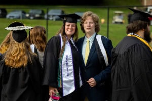 A student in a cap and gown smiles for a photo with a family member