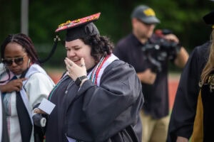 A student smiles and holds her hand to her mouth during Commencement 