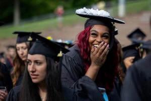 A student smiles and holds her hand to her mouth during Commencement 