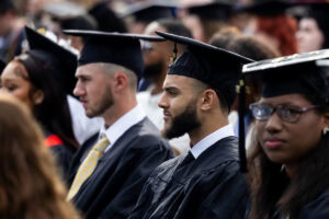 Students sit in the crowd in their caps and gowns during Commencement 