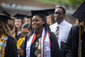 A student wearing a cap and gown smiles during the 2025 Commencement ceremony 