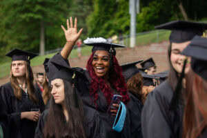 A student in a cap and gown smiles and waves from the crowd during Commencement 