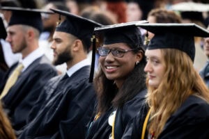 Students, in their caps and gowns, smile in the crowd during their Commencement ceremony