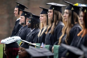 Students, in their caps and gowns, smile in the crowd during their Commencement ceremony