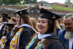 Students, in their caps and gowns, smile in the crowd during their Commencement ceremony