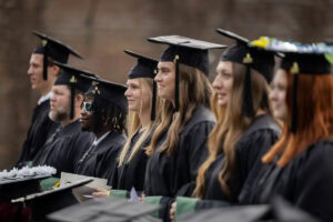Students, in their caps and gowns, smile in the crowd during their Commencement ceremony