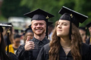 Students, in their caps and gowns, smile in the crowd during their Commencement ceremony