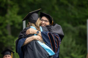 Professor Peggy Schimmoeller hugs a graduate student onstage during Commencement after they received their hood 