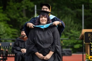 A graduate student receives their hood onstage during Commencement
