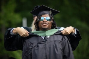 A graduate student receives their hood onstage during Commencement
