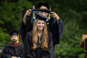 A graduate student receives their hood onstage during Commencement