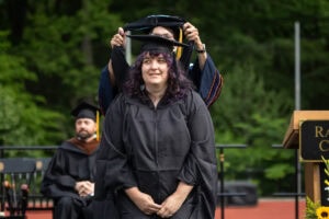 A graduate student receives their hood onstage during Commencement