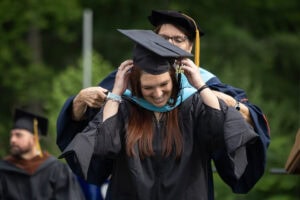 A graduate student receives their hood onstage during Commencement