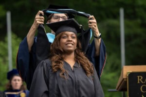 A graduate student receives their hood onstage during Commencement