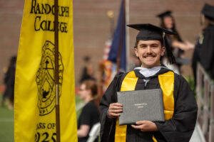 A graduate in a cap and gown poses with his diploma after exiting the stage 