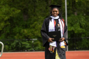 A graduate in a cap and gown smiles with her diploma after exiting the stage 