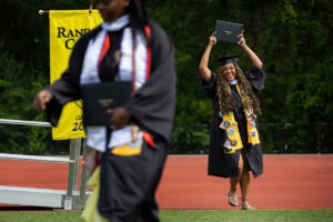 A student holds her diploma high in the air, celebrating, after exiting the Commencement stage