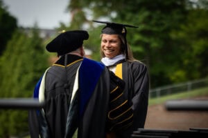 A graduate in a cap and gown smiles while receiving her diploma from President Sue Ott Rowlands