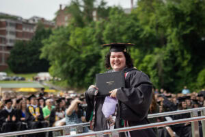 A graduate in a cap and gown smiles with her diploma after exiting the stage 