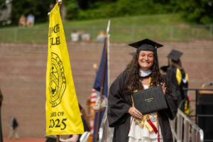 A graduate in a cap and gown smiles with her diploma after exiting the stage 