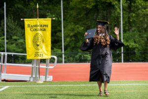 A graduate in a cap and gown smiles and waves to the crowd with her diploma after exiting the stage 