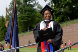 A graduate in a cap and gown smiles with her diploma after exiting the stage 
