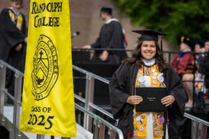 A graduate in a cap and gown smiles with her diploma after exiting the stage 