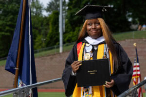 A graduate in a cap and gown smiles with her diploma after exiting the stage 