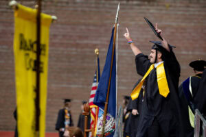 A student holds his diploma up in the air onstage during Commencement, while looking out at the crowd