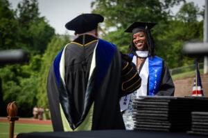 A graduate in a cap and gown receives her diploma from President Sue Ott Rowlands
