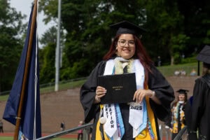 A graduate in a cap and gown smiles with her diploma after exiting the stage 