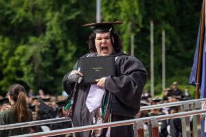 A graduate in a cap and gown smiles with her diploma after exiting the stage 