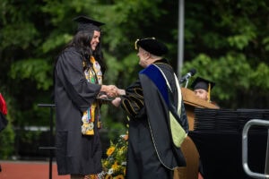A graduate in a cap and gown smiles while receiving her diploma from President Sue Ott Rowlands