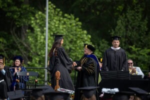 A graduate in a cap and gown receives her diploma from President Sue Ott Rowlands