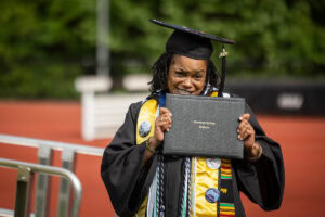 Sonia Langhorne '25 poses with her diploma, smiling and holding it up by her face 