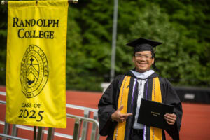 A student smiles and poses with his diploma after exiting the stage 
